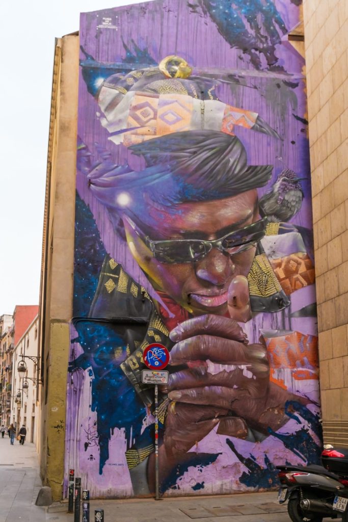 A three-story mural on the side of a building of a man wearing a black hat and sunglasses.