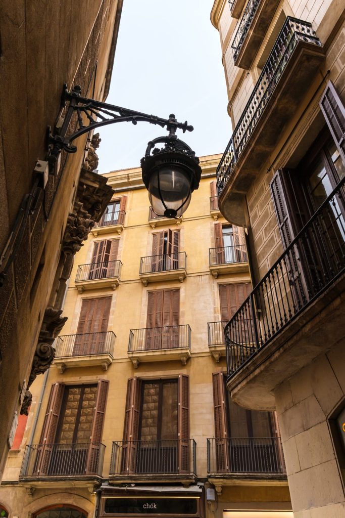 A view of an old building between two other buildings on either side with balconies and an old street lamp hanging above.