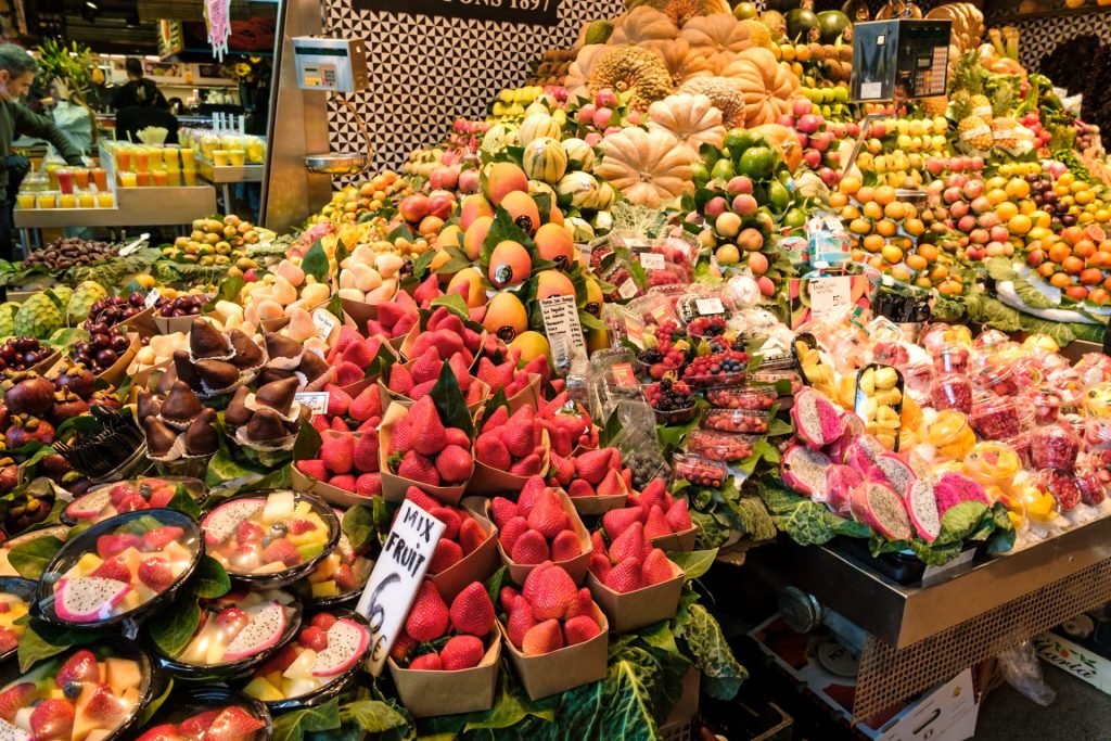 Strawberries, mangoes, mangosteens, apricots, dragonfruit, and cut fruit on display for sale in La Boqueria Market.